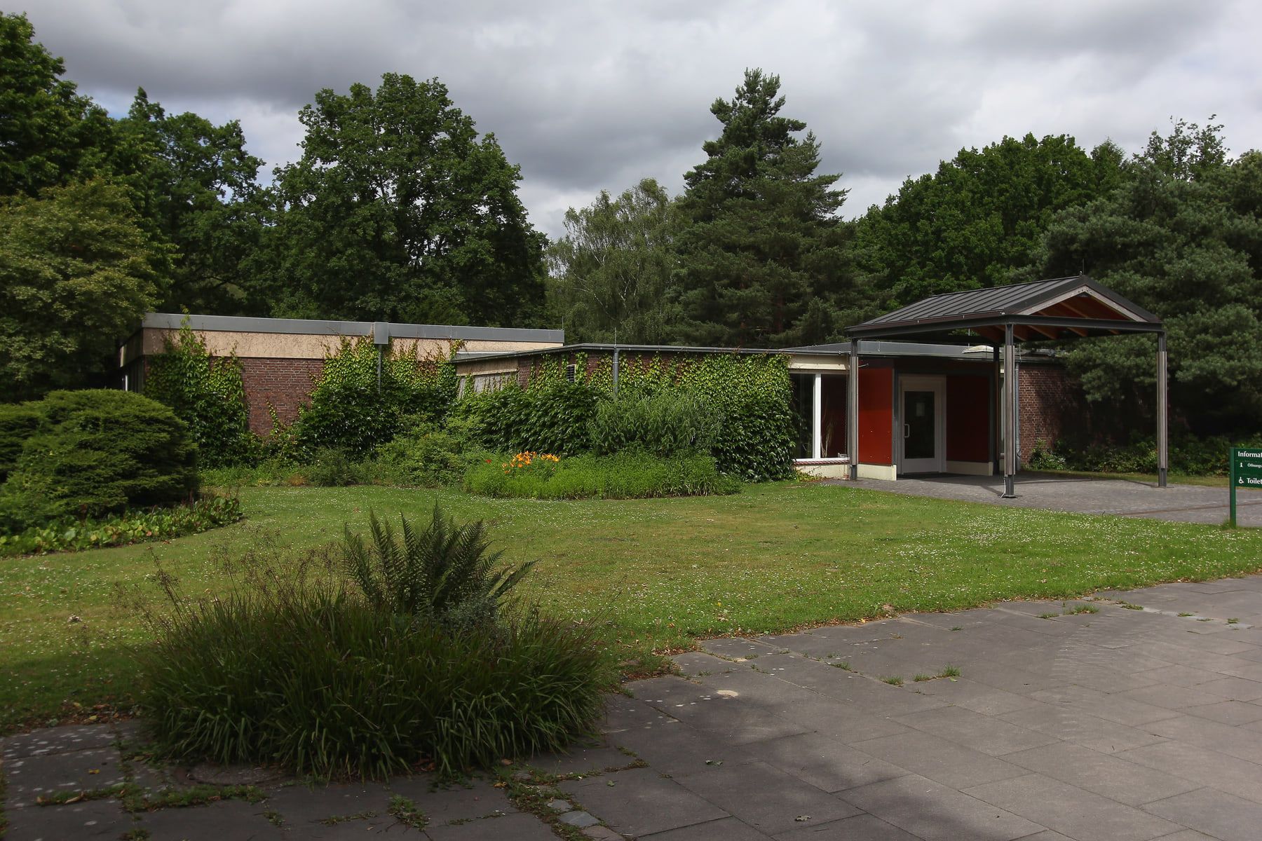 Niedriges Backsteingebäude mit weit auskragendem Eingangsdach an einer Rasenfläche auf Friedhof Öjendorf